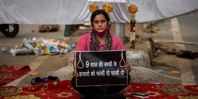 Tina Verma, 27, a social activist, holds a placard which reads, "Hang the killers of 9-year old child" at a demonstration site outside a crematorium where a 9-year-old girl from the lowest rung of India's caste system was, according to her parents and protesters, raped and killed earlier this week, in New Delhi, India, Thursday, Aug. 5, 2021. (AP Photo/Altaf Qadri)