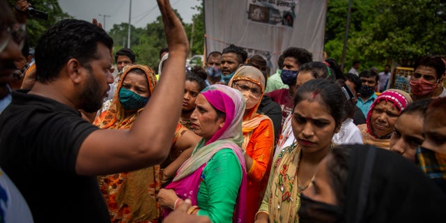 A man tries to calm protesters down as they try to block a street outside a crematorium where a 9-year-old girl from the lowest rung of India's caste system was, according to her parents and protesters, raped and killed earlier this week, in New Delhi, India, Thursday, Aug. 5, 2021. (AP Photo/Altaf Qadri)