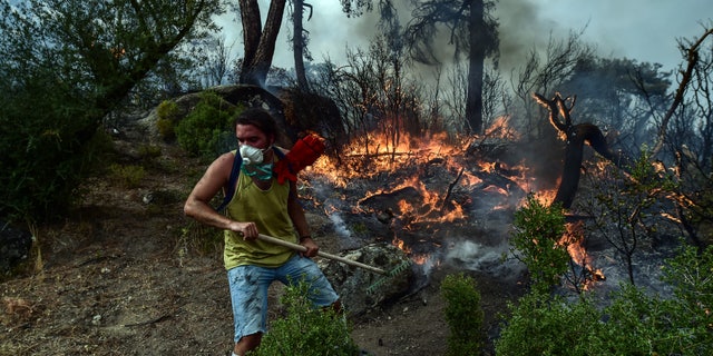A volunteer works to put out a fire in Yatagan, Mugla province, Turkey on Friday, August 6, 2021. Thousands of people fled uncontrollable forest fires in Greece and Turkey on Friday, as a long heat wave turned forests into powder magazines that threatened populated areas, electrical installations and historic sites. (Ismail Coskun / IHA via AP)