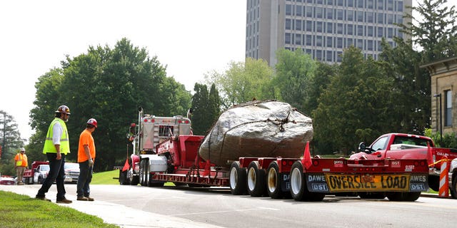 A flatbed trailer pulls away from Observatory Hill with Chamberlin Rock in tow in Madison, Wisconsin on Friday, August 6, 2021. The University of Wisconsin is removing the 70-ton rock from its Madison campus at the request of minority students who see the rock as a symbol of racism.  Chamberlin Rock, at the top of Observatory Hill, is named after Thomas Crowder Chamberlin, geologist and former university president.  (Kayla Wolf / Wisconsin State Journal via AP)