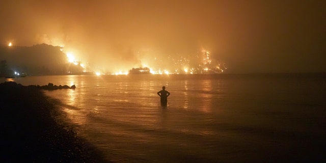 A man watches the flames as wildfire approaches Kochyli beach near Limni village on the island of Evia, about 160 kilometers (100 miles) north of Athens, Greece, late Friday, Aug. 6, 2021. Wildfires raged uncontrolled through Greece and Turkey for yet another day Friday, forcing thousands to flee by land and sea, and killing a volunteer firefighter on the fringes of Athens in a huge forest blaze that threatened the Greek capital's most important national park. (AP Photo/Thodoris Nikolaou)