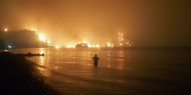 A man watches the flames as a forest fire approaches Kochyli beach near the village of Limni on the island of Evia, about 160 kilometers (100 miles) north of Athens, Greece, Friday August 6, 2021. another day Friday, forcing thousands to flee by land and sea, and killing a volunteer firefighter on the outskirts of Athens in a massive forest fire that threatened the most important national park in the Greek capital. (AP Photo / Thodoris Nikolaou)