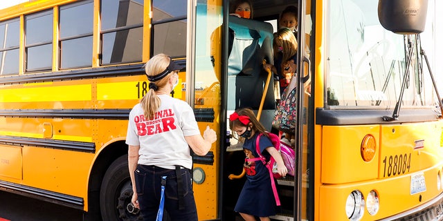 教師が2021年8月9日月曜日ネバダ州ヘンダーソンにある新しいHannah Marie Brown小学校で登校初日バスで降りて学生たちを迎えています。 全国で5番目に大きい地域の対面授業に復帰する学生30万人余りと教師1万8000人余りのためにマスクが必要だった。  （APによるYasmina Chavez / Las Vegas Sun）