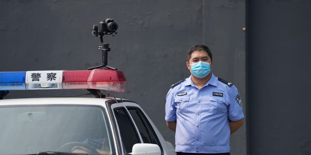 A policeman wearing a face mask stands guard next to a police vehicle with a camera outside a detention center where Dominic Barton, ambassador of Canada to China will meet Canadian Michael Spavor, in Dandong, China, Wednesday, Aug. 11, 2021. A Chinese court has sentenced Michael Spavor to 11 years on spying charges in case linked to Huawei. (AP Photo/Ng Han Guan)