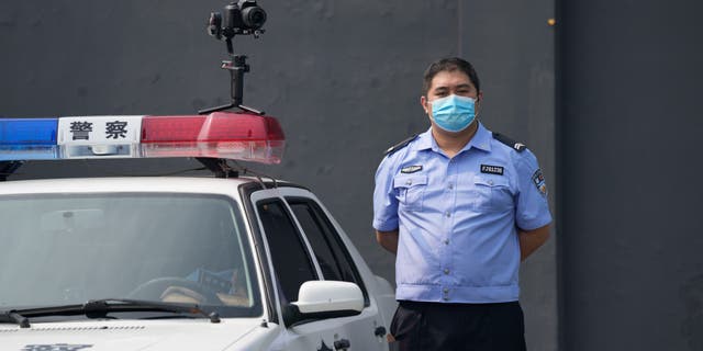 A policeman wearing a face mask stands guard next to a police vehicle with a camera outside a detention center where Dominic Barton, ambassador of Canada to China will meet Canadian Michael Spavor, in Dandong, China, Wednesday, Aug. 11, 2021. A Chinese court has sentenced Michael Spavor to 11 years on spying charges in case linked to Huawei. (AP Photo/Ng Han Guan)
