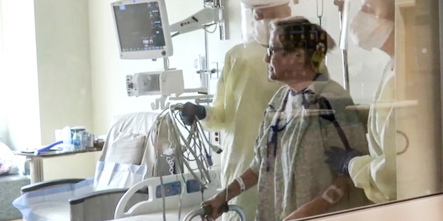 Coronavirus patient Joan Bronson walks across her hospital room with the help of a physical therapist at Ochsner Medical Center in the New Orleans suburb of Jefferson, La., on Tuesday, Aug.11, 2021. (AP Photo/Stacey Plaisance)