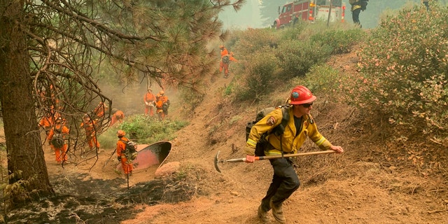 CalFire firefighters and California Correctional Center (CCC) inmates fight a spot fire on the side of Highway CA-36 between Chester and Westwood in Plumas County, Calif., Friday, Aug. 13, 2021. In California, the Dixie Fire that virtually destroyed the Sierra Nevada town of Greenville is less than a third surrounded. Fire officials say Northern California will have dangerous fire weather on Friday, including possible lightning that could spark more blazes. Climate change has made the U.S. West warmer and drier in the past 30 years and will continue to make the weather more extreme and wildfires more destructive, according to scientists. (AP Photo/Eugene Garcia)