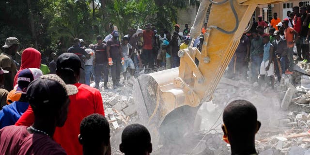 People watch a bulldozer remove debris at the collapsed Le Manguier hotel in Les Cayes, Haiti, Monday, Aug. 16, 2021, two days after a 7.2-magnitude earthquake struck the southwestern part of the country. (AP Photo/Matias Delacroix)