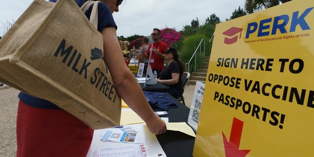 People sign forms to oppose vaccine passports when participating in the "California SOS Vaccine Free Passport Rally" at Tongva Park in Santa Monica, Calif. on Saturday.  A vaccine worker was struck by a motorist in San Clarita, which may have been intentional, authorities said.  (AP Photo / Damian Dovarganes)