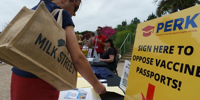 People sign forms to oppose vaccine passports as they participate at the "S.O.S California No Vaccine Passport Rally" at Tongva Park in Santa Monica, Calif., on Saturday. A vaccine worker was struck by a motorist in San Clarita that may have been intentional, authorities said. (AP Photo/Damian Dovarganes)