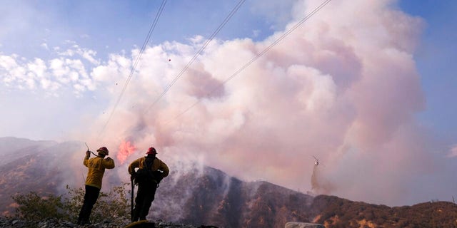 Firefighters watch as a helicopter drops water at the South Fire burning in Lytle Creek, San Bernardino County, north of Rialto, カリフォルニア, 水曜日, 8月. 25, 2021. 