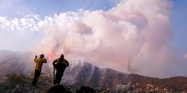 Firefighters watch as a helicopter drops water at the South Fire burning in Lytle Creek, San Bernardino County, north of Rialto, カリフォルニア, 水曜日, 8月. 25, 2021.