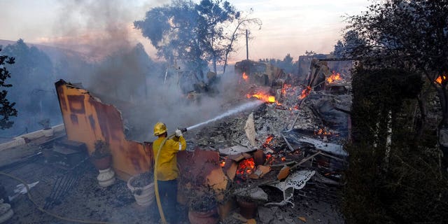 A firefighter tries to extinguish the flames at a burning house as the South Fire burns in Lytle Creek, San Bernardino County, north of Rialto, カリフォルニア, 水曜日, 8月. 25, 2021.