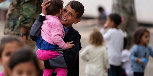 A recently evacuated young Afghan boy carries a child at the Ramstein U.S. Air Base, Germany, Tuesday, Aug. 24, 2021. The largest American military community overseas housed thousands of Afghan evacuees in an increasingly crowded tent city. (Associated Press)