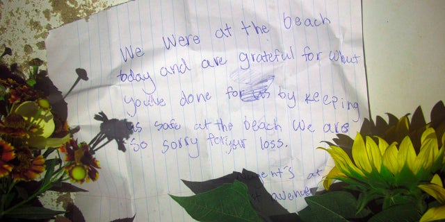 A note left with flowers is seen placed by a lifeguard chair on the sand at the beach in Berkeley Township, N.J., where a young lifeguard was killed and seven others injured by a lightning strike, Monday, Aug. 30, 2021. (AP Photo/Wayne Parry)