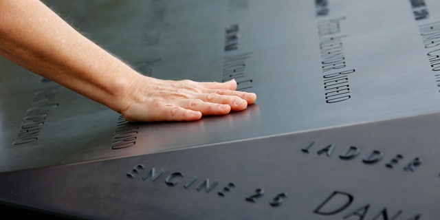A woman places her hand on a name etched in the wall of one of the pools at the 9/11 memorial plaza in the World Trade Center site in New York Monday, Sept. 12, 2011, on the first day that the memorial was opened to the public. (AP Photo/Mike Segar, Pool)