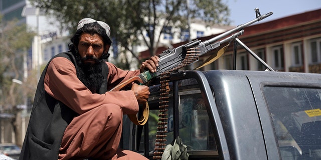 A Taliban fighter sits on the back of a vehicle with a machine gun in front of the main gate leading to the Afghan presidential palace, in Kabul, Afghanistan, Monday, Aug. 16, 2021.