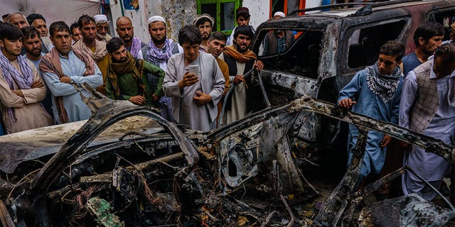 People gather around the incinerated husk of a vehicle that was destroyed by a U.S. drone strike in Kabul, Afghanistan, on Aug. 29, 2021.
