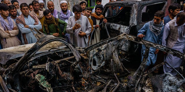 People gather around the incinerated husk of a vehicle that was destroyed by a U.S. drone strike in Kabul, Afghanistan, on Aug. 29, 2021.