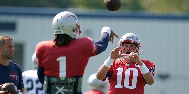 New England Patriots quarterback Cam Newton (1) passes the ball to Patriots quarterback Mac Jones (10) during a joint NFL football practice with the New York Giants, 星期四, 八月. 26, 2021, (福克斯伯勒), 弥撒. (AP Photo/Steven Senne)
