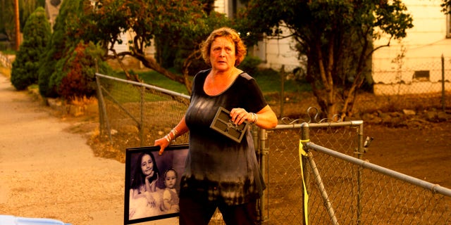 Rose Mooney carries photos from her home, which is under an evacuation warning, as the Dixie Fire burns towards Susanville, Calif., on Monday, Aug. 16, 2021.