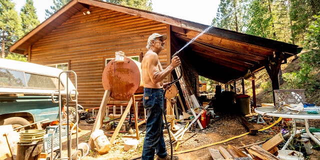 Dan Santos sprays water while defending his girlfriend's Greenville home as the Dixie Fire burns nearby in Plumas County, Calif., on Tuesday, Aug. 3, 2021. Dry and windy conditions have led to increased fire activity as firefighters battle the blaze which ignited July 14.