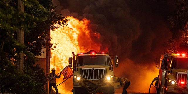 A firefighter saves an American flag as flames consume a home during the Dixie fire in Greenville, California on August 4, 2021. - The Dixie fire burned through dozens of homes and businesses in downtown Greenville and continues to forge towards other residential communities. Officials in northern California on August 4, 2021 warned residents of two communities in the path of the raging Dixie fire to evacuate immediately as high winds whipped the flames onwards. (Photo by JOSH EDELSON / AFP) (Photo by JOSH EDELSON/AFP via Getty Images)