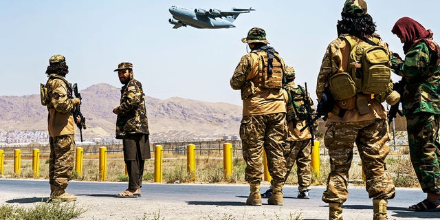 KABUL, AFGHANISTAN - AUG 29, 2021: A C-17 Globemaster takes off as Taliban fighters secure the outer perimeter alongside the US side of Hamid Karzai International Airport in Kabul, Afghanistan, Sunday August 29, 2021. (MARCUS YAM / LOS ANGELES TIMES)