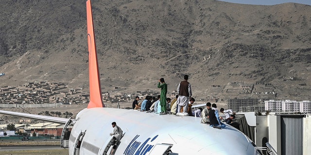 Afghan people climb atop a plane as they wait at the Kabul airport in Kabul on August 16, 2021, after a stunningly swift end to Afghanistan's 20-year war, as thousands of people mobbed the city's airport trying to flee the group's feared hardline brand of Islamist rule. 