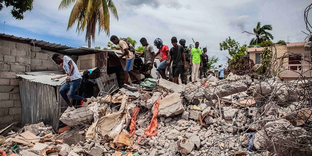 People walk over a pile of rubble from a collapsed building after a 7.2-magnitude earthquake struck Haiti on August 16, 2021 in Les Cayes, Haiti. Rescue workers have been working among destroyed homes since the quake struck on Saturday and so far there are 1,297 dead and 5.700 wounded. The epicenter was located about 100 miles west of the capital city Port-au-Prince. 