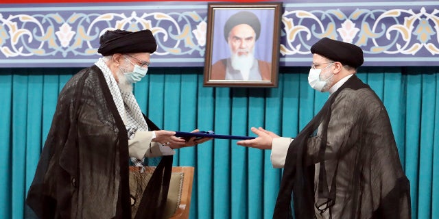 De hoogste leider van Iran, ayatollah Ali Khamenei, links, geeft dinsdag zijn officiële stempel van goedkeuring aan de nieuw gekozen president Ebrahim Raisi tijdens een goedkeuringsceremonie in Teheran, Iran.  Op de achtergrond hangt een portret van de overleden revolutionaire oprichter Ayatollah Khomeini.  (Bureau van de hoogste leider van Iran/The Associated Press)