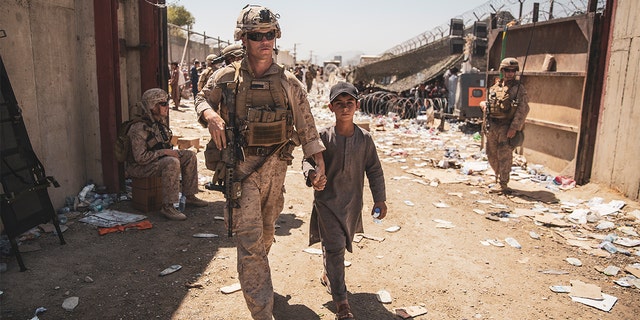 A U.S. Marine with the Special Purpose Marine Air-Ground Task Force-Crisis Response-Central Command (SPMAGTF-CR-CC) escorts a kid to his family during an evacuation at Hamid Karzai International Airport, Kabul, Afghanistan, Aug. 24. U.S. service members and coalition forces are assisting the Department of State with a non-combatant evacuation operation (NEO) in Afghanistan. 