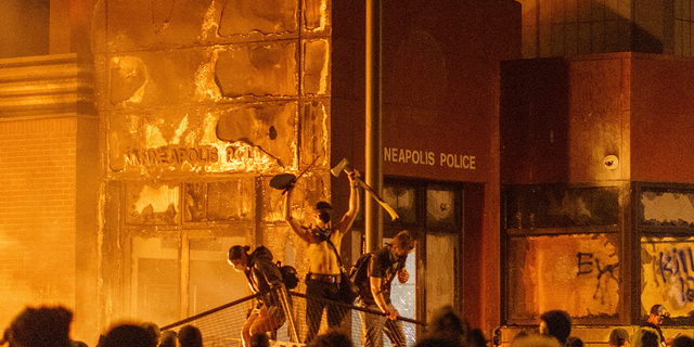 Flames from a nearby fire illuminate protesters standing on a barricade in front of the Third Police Precinct on May 28, 2020 in Minneapolis, Minnesota, during a protest over the death of George Floyd.