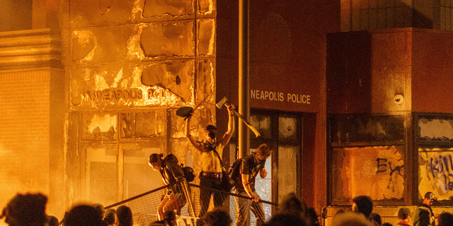 Flames from a nearby fire illuminate protesters standing on a barricade in front of the Third Police Precinct on May 28, 2020 in Minneapolis, Minnesota, during a protest over the death of George Floyd.