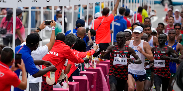 Competitors walk past the water station during the men's marathon of the 2020 Summer Olympics on Sunday, August 8, 2021, in Sapporo, Japan.