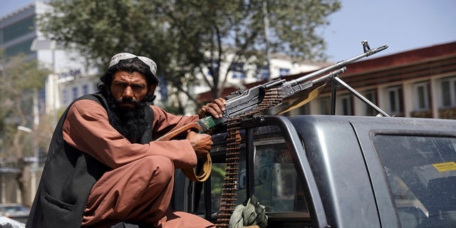 A Taliban fighter sits on the back of a vehicle with a machine gun in front of the main gate leading to the Afghan presidential palace, in Kabul, Afghanistan, on Monday. (AP)