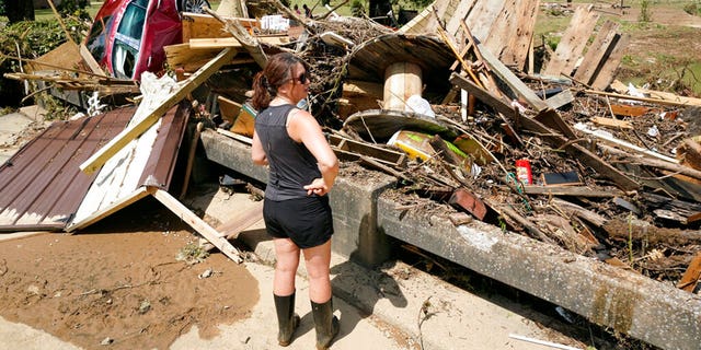 A woman looks at debris washed up against a bridge over a stream Sunday, Aug. 22, 2021, in Waverly, Tenn. Heavy rains caused flooding Saturday in Middle Tennessee and have resulted in multiple deaths as homes and rural roads were washed away.