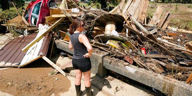 A woman looks at debris washed up against a bridge over a stream Sunday, Aug. 22, 2021, in Waverly, Tenn. Heavy rains caused flooding Saturday in Middle Tennessee and have resulted in multiple deaths as homes and rural roads were washed away.