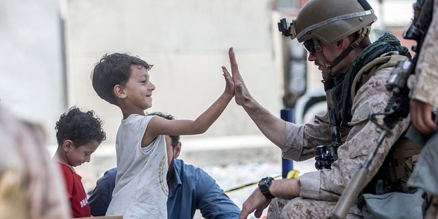 In this Aug. 22, 2021, image provided by the U.S. Marine Corps, A Marine with Special Purpose Marine Air-Ground Task Force-Crisis Response-Central Command gives a high five to a child during an evacuation at Hamid Karzai International Airport in Kabul, Afghanistan. Sgt. Samuel Ruiz/U.S. Marine Corps via AP)