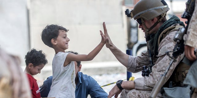 In this Aug. 22, 2021, image provided by the U.S. Marine Corps, A Marine with Special Purpose Marine Air-Ground Task Force-Crisis Response-Central Command gives a high five to a child during an evacuation at Hamid Karzai International Airport in Kabul, Afghanistan. Sgt. Samuel Ruiz/U.S. Marine Corps via AP)