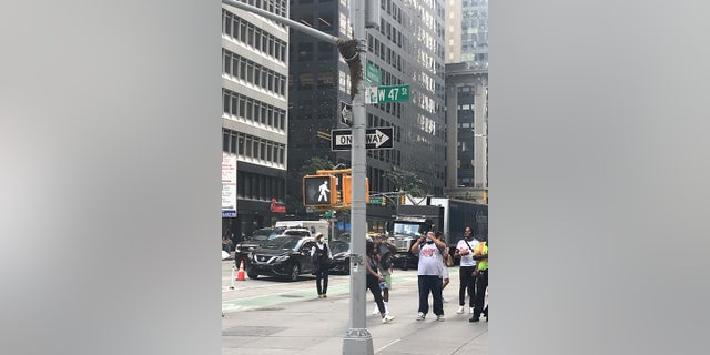 Onlookers gather Tuesday to watch a large colony of bees gather around a light pole in midtown Manhattan.