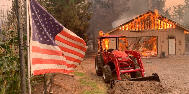 A red tractor is left behind as a home burns outside of Taylorsville in Plumas County, Calif., that was impacted by the Dixie Fire on Friday. (AP Photo/Eugene Garcia)