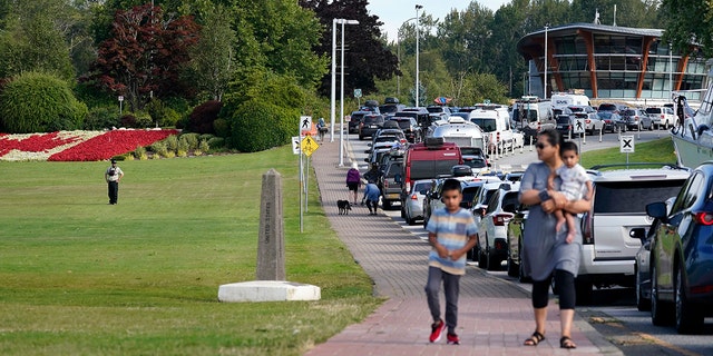 A Canadian border official, left, looks on at a line of vehicles waiting to enter Canada at the Peace Arch border crossing Monday, Aug. 9, 2021, in Blaine, Wash. Canada lifted its prohibition on Americans crossing the border to shop, vacation or visit, but America kept similar restrictions in place, part of a bumpy return to normalcy from coronavirus travel bans. (AP Photo/Elaine Thompson)