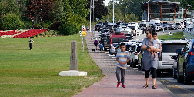 A Canadian border official, left, looks on at a line of vehicles waiting to enter Canada at the Peace Arch border crossing Monday, Aug. 9, 2021, in Blaine, Wash. Canada lifted its prohibition on Americans crossing the border to shop, vacation or visit, but America kept similar restrictions in place, part of a bumpy return to normalcy from coronavirus travel bans. (AP Photo/Elaine Thompson)