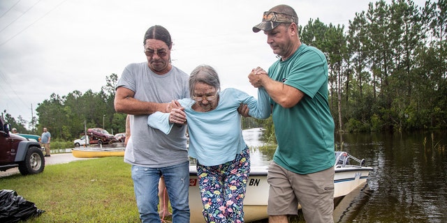 Stanley Delle, left, and Jeff Delle help 80-year-old Eileen Delle onto dry land Monday, Aug. 30, 2021 after floodwaters from Hurricane Ida surrounded her elevated home in the Shoreline Park community in Bay St. Louis. 