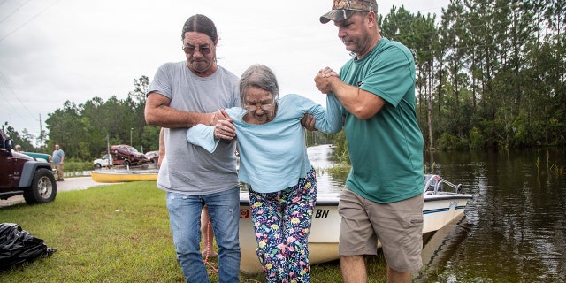 Stanley Delle, left, and Jeff Delle help 80-year-old Eileen Delle onto dry land Monday, Aug. 30, 2021 after floodwaters from Hurricane Ida surrounded her elevated home in the Shoreline Park community in Bay St. Louis.