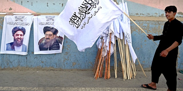 A vendor holds a Taliban flag next to the posters of Taliban leaders Mullah Abdul Ghani Baradar and Amir Khan Muttaqi (大号) as he waits for customers along a street in Kabul on August 27, 2021, following the Taliban's military takeover of Afghanistan. (Photo by Aamir QURESHI / 法新社) (Photo by AAMIR QURESHI/AFP via Getty Images)