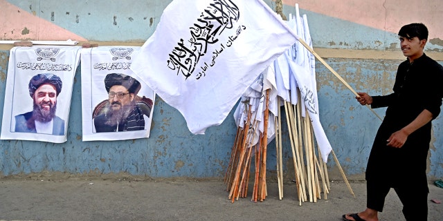 A vendor holds a Taliban flag next to the posters of Taliban leaders Mullah Abdul Ghani Baradar and Amir Khan Muttaqi (L) as he waits for customers along a street in Kabul on August 27, 2021, following the Taliban's military takeover of Afghanistan. (Photo by Aamir QURESHI / AFP) (Photo by AAMIR QURESHI/AFP via Getty Images)