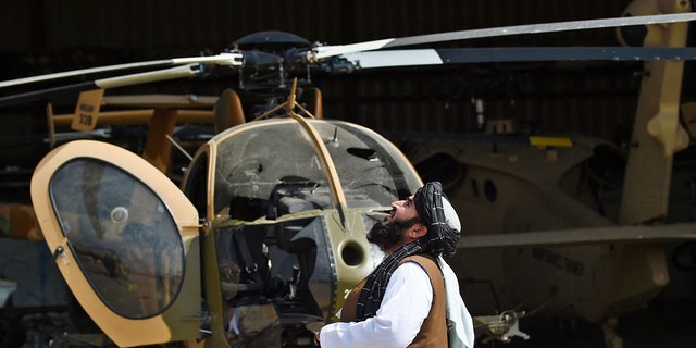 A Taliban member looks up near a damaged helicopter at the airport in Kabul on Tuesday. (AFP via Getty Images)