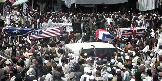 Crowds carry makeshift coffins draped in NATO, US and Union Jack flags during a mock funeral on a street in Khost, Afghanistan on August 31, 2021, in this capture of screen obtained from a video on social networks.  ZHMAN TV / via REUTERS 
